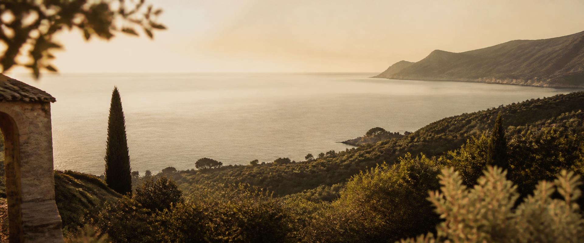 Costa mediterránea al atardecer con cipreses y colinas de olivos